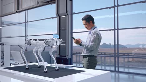 vista lateral completa del cuerpo de un trabajador profesional masculino asiático de pie con su teléfono en una fábrica de alta tecnología, perro robot, trabajando continuamente con su teléfono