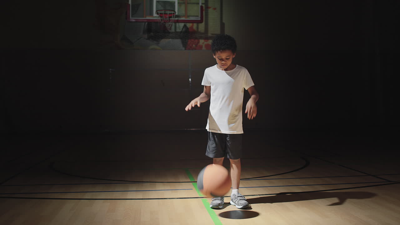 Cute Boy Dribbling Ball on Dark Basketball Court