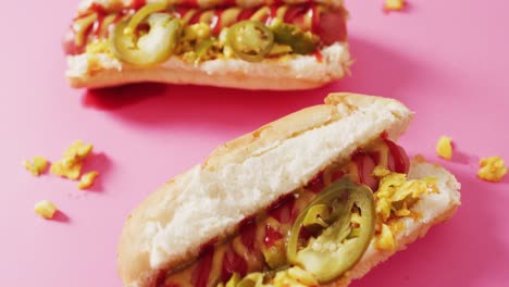 video of hot dogs with mustard, ketchup and jalapeno on a pink surface