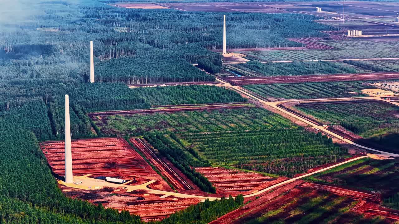 Three wind turbine towers rise amid cleared land, roads, and forest during large-scale construction