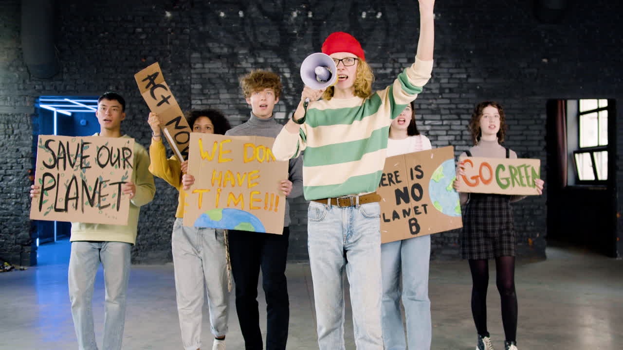vista frontal de jóvenes activistas ambientales con pancartas y megáfonos caminando hacia la cámara y protestando contra la inacción del cambio climático