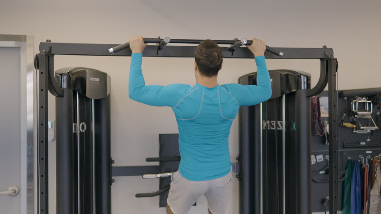 hombre francés en el gimnasio haciendo ejercicio en la barra de tracción, haciendo tracción de agarre ancho para fortalecer la espalda y el hombro