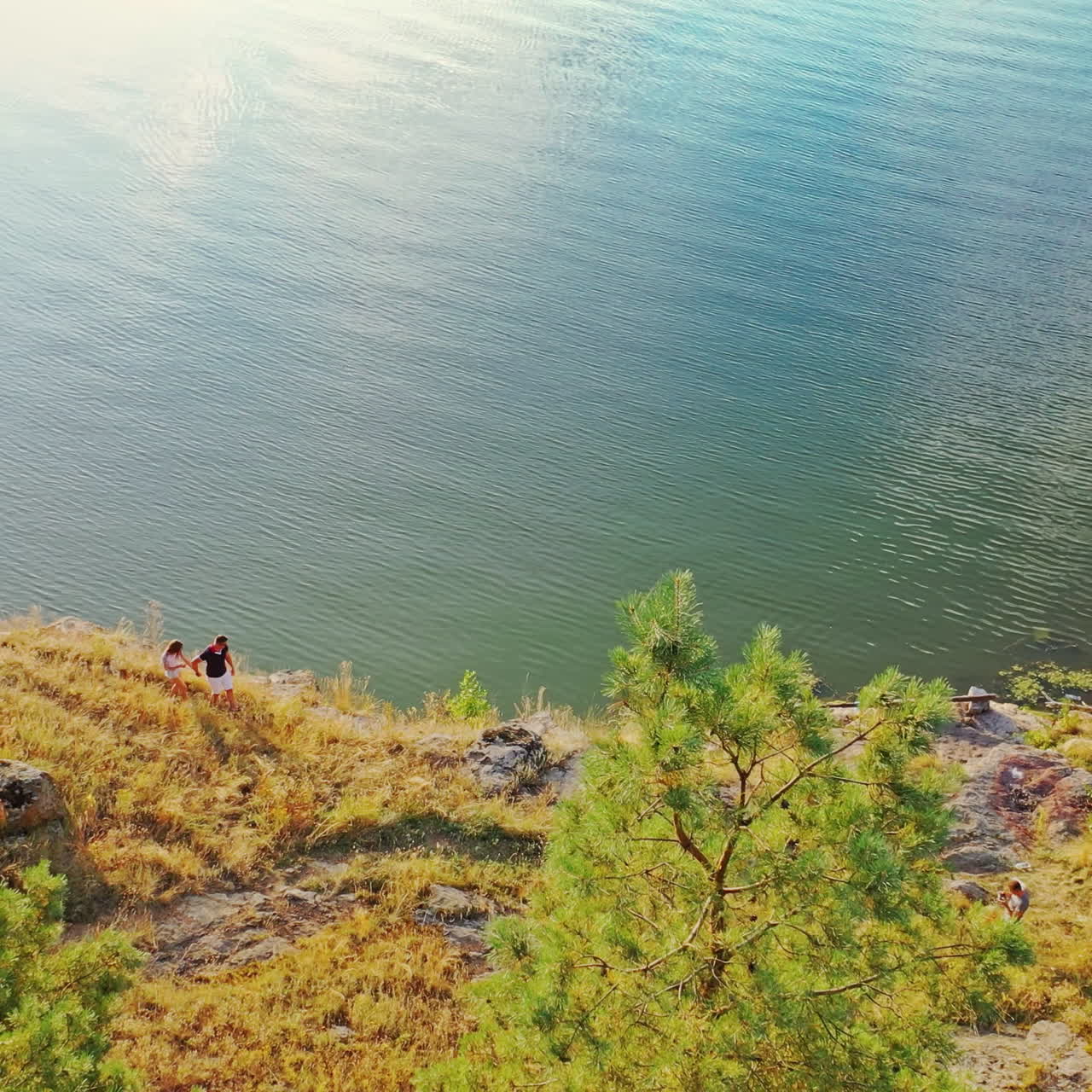 View from above on two young people walking near water. Drone view on a beautiful natural landscape and a man with a woman holding hands enjoying together near the river.