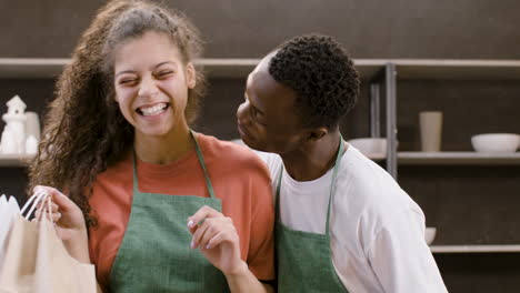 close up view of two co workers at a pottery store posing in front of the camera while smiling and hugging each other