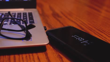 Slider shot panning left to right with glasses on top of a laptop computer and a cell phone to the right laying on a table