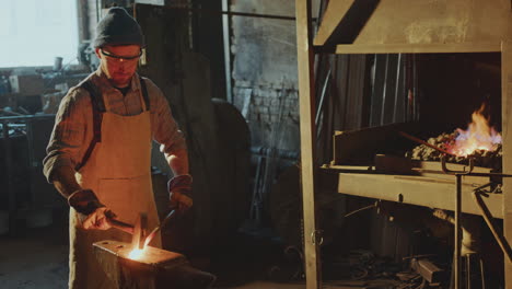 blacksmith beating hot metal with sledgehammer on anvil in workshop