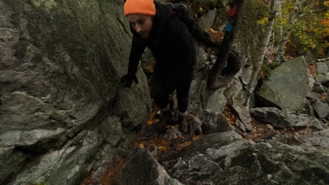 young man is tired from climb up rocks in colorful fall forest, handheld pan