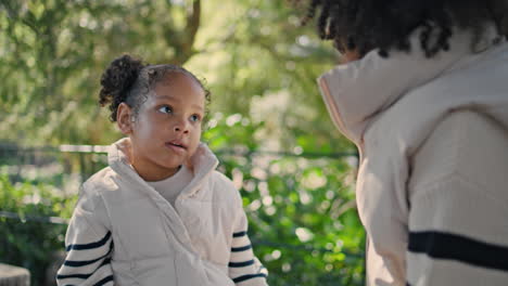 little girl spending time with mother sitting on bench green garden close up.