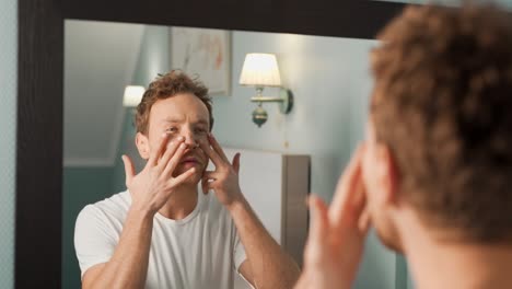 handsome man applying cream on face in front of a mirror