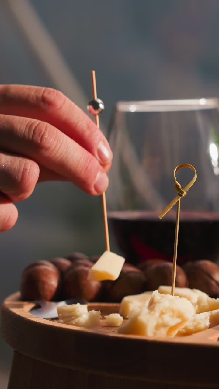 Man holds cheese on skewer at low coffee table closeup. Assortment of delicious appetizers on small wooden table for gourmets. Snack plate to enjoy wine