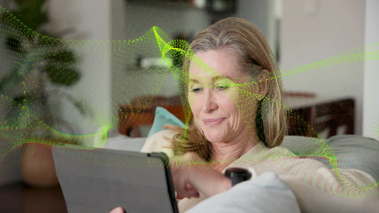 Woman tapping tablet, shifting upright to recline on sofa, green wave flowing over woman for tech