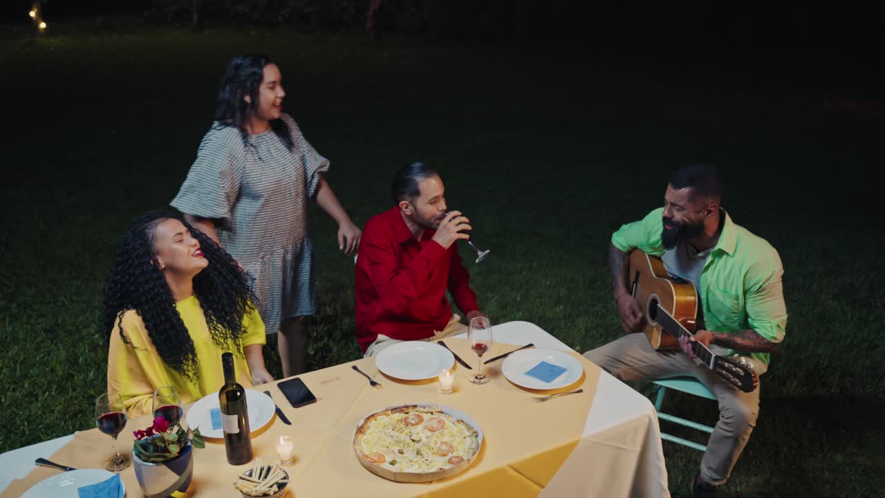 Friends Enjoying Outdoor Dinner Party with Live Music and Singing at Night