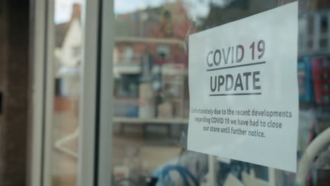 covid19 closed shop window with public notice on display and empty high-street in reflection