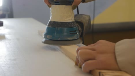 a woman carpenter in the workshop grinds a wooden block with a grinder. the carpenter's woman has green nail polish.