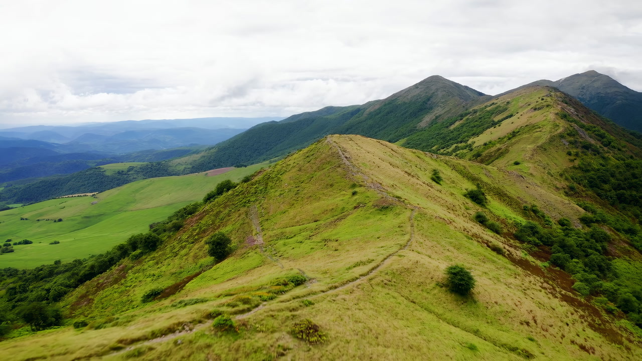 Aerial Ridge Panorama Overcast Sky Green Hills, Windswept Trail Tracing Ridge Line, Distant Peaks Shrouded