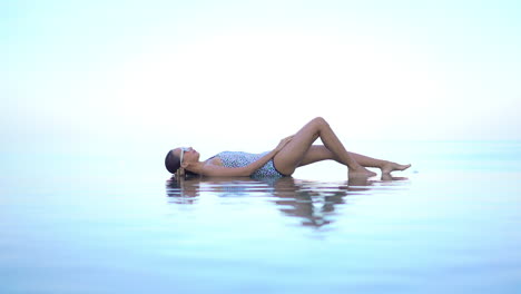 Mujer-En-Traje-De-Baño-Acostada-En-El-Borde-De-La-Piscina-Infinita-Que-Se-Fusiona-Con-El-Horizonte-Marino-Y-El-Cielo