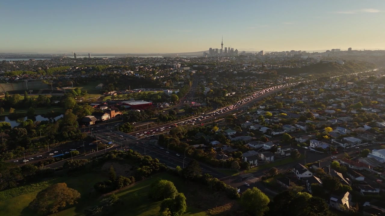 Veduta aerea di Auckland all'alba, che rivela la Sky Tower, i sobborghi estesi e il traffico intenso dell'autostrada nella calda luce del mattino
