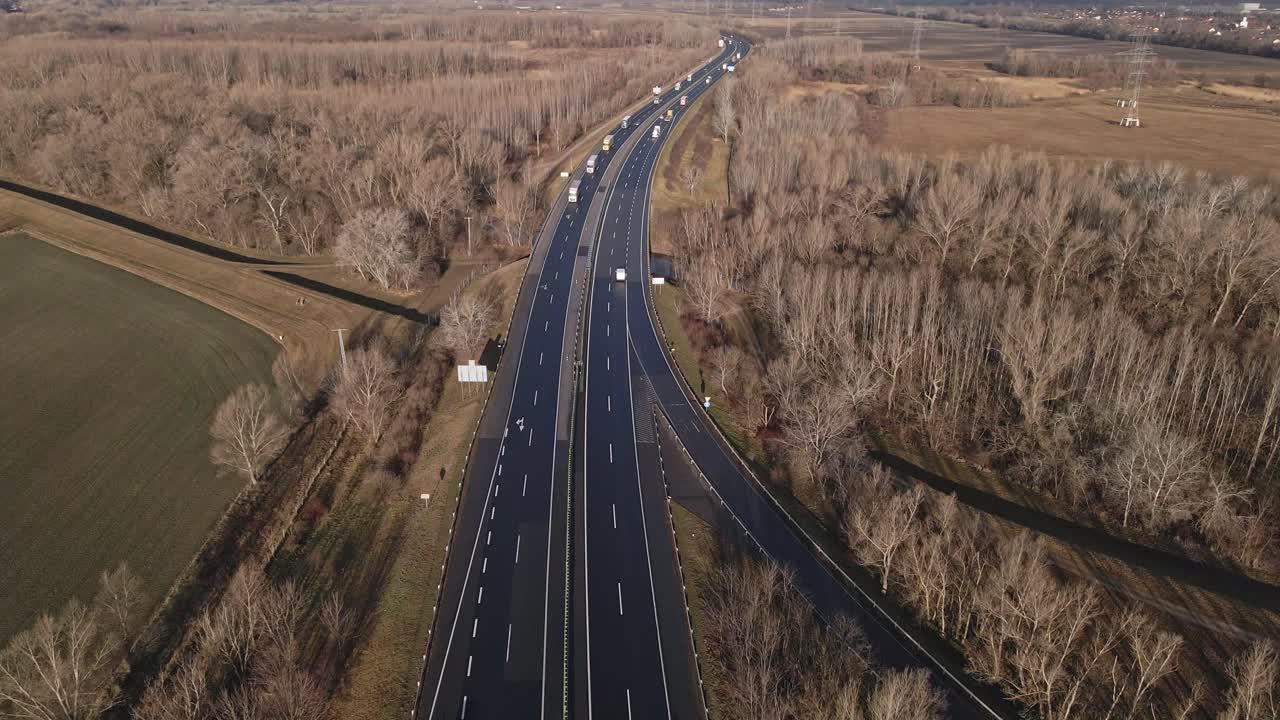 Aerial video of highway with trucks and cars in winter landscape with flying forward drone.