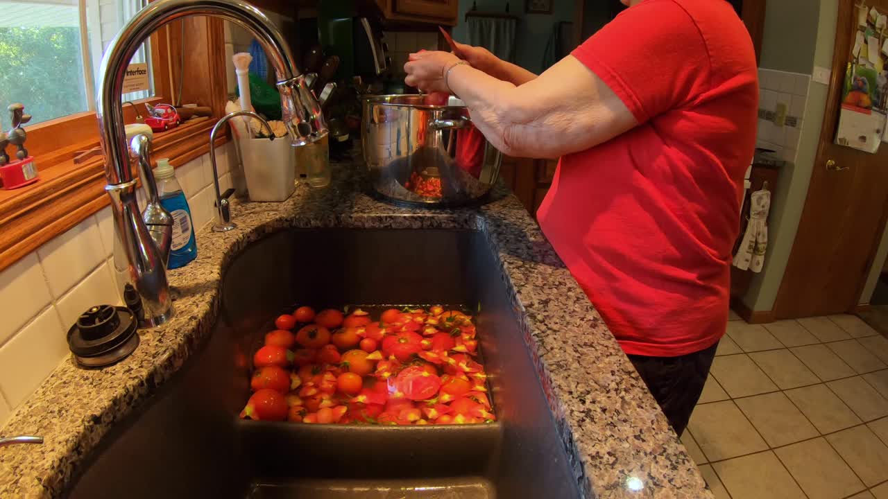 통조림을 위해 정원 재배 토마토를 준비하는 동안 부엌 싱크대에 서있는 나이든 여자