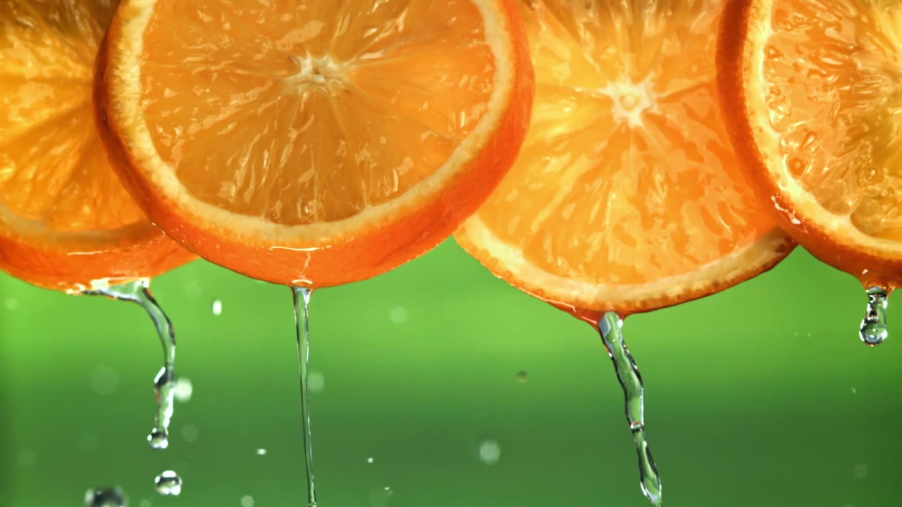 Erfrischendes Wasser tropft von frischen Orangenscheiben auf grünem Hintergrund