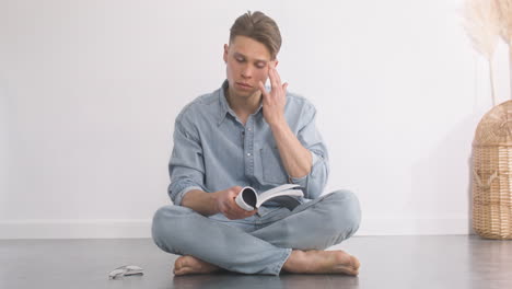 hombre guapo limpiando sus lágrimas mientras lee un libro en el suelo