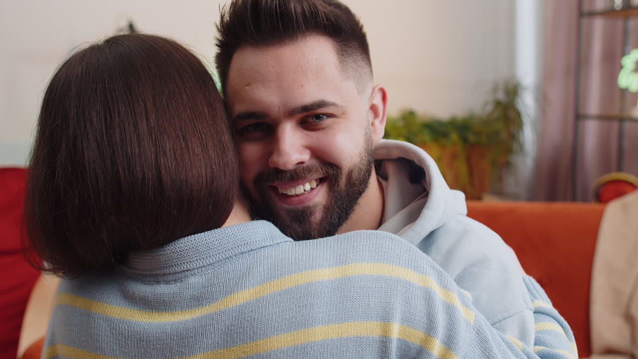 Portrait of man embracing hugging woman looking at camera over her shoulder at home room support