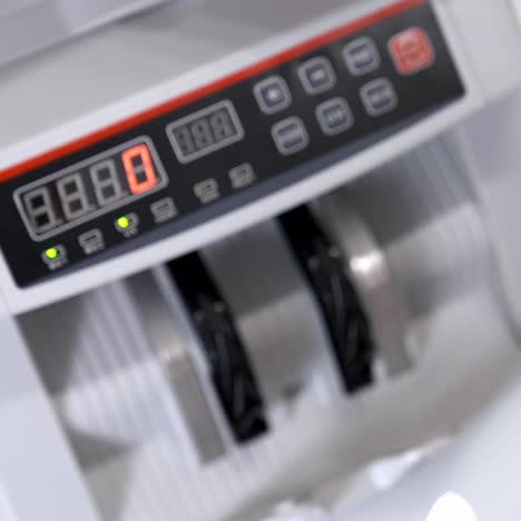 woman holding money near counting machine at table indoors, closeup