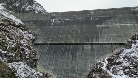 asombrosas imágenes de drones sobre un lago alpino, una represa hidroeléctrica y un vasto embalse alpino bordeado por montañas escarpadas con un sendero junto al agua después de una ligera caída de nieve