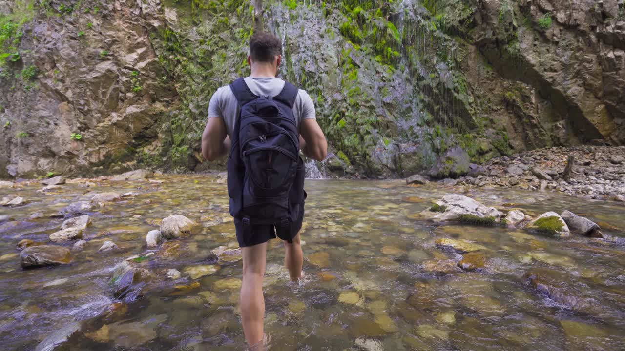 hombre caminando descalzo en stony creek. hay una cascada.