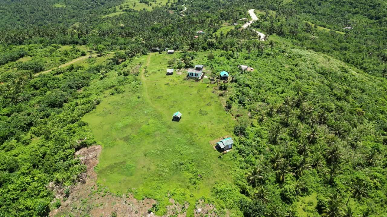campo de granja remoto con graneros simples en un claro de bosque tropical, inclinación aérea hacia abajo