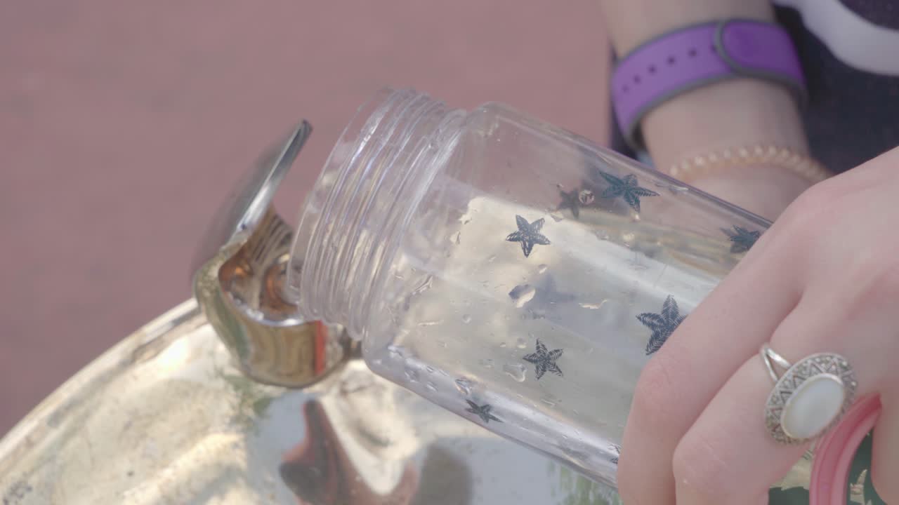 더운 날씨에 분수대에서 물병을 채우는 여자