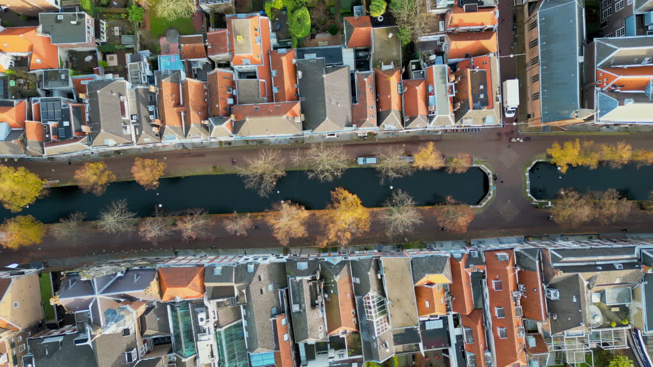 Aerial drone view of a narrow canal flanked by rows of historic Dutch townhouses with red-tiled roofs and tree-lined walkways in Delft, Netherlands