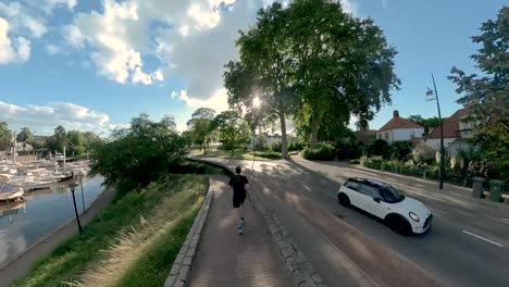 Following-middle-aged-male-trail-runner-along-recreational-port-and-boulevard-of-Dutch-city-Zutphen-with-sunlight-shining-through-tree-tops