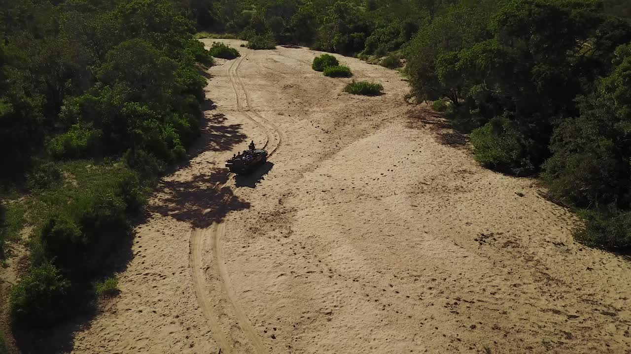una toma de un drone de un vehículo de safari conduciendo en un lecho de río secado en áfrica