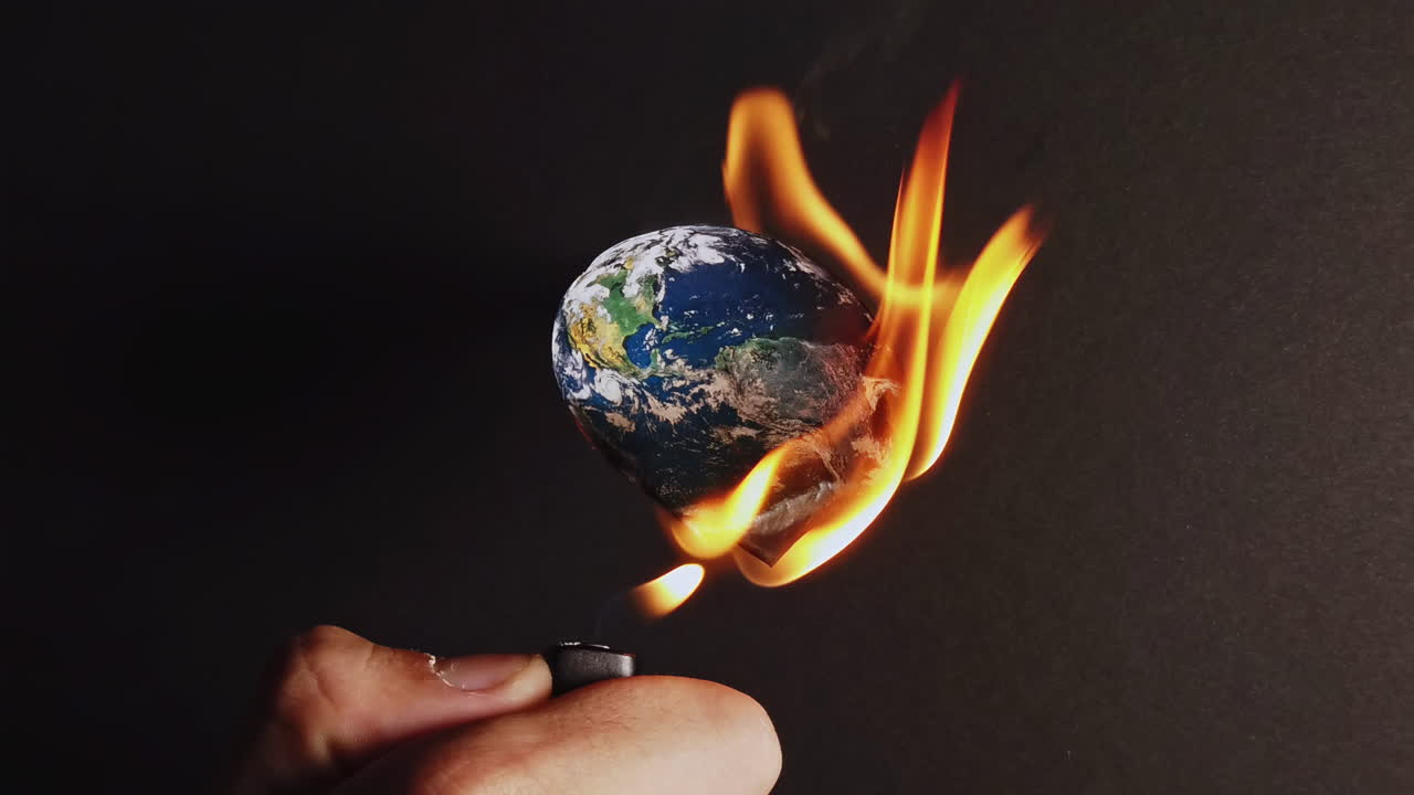 Man hand burns with a lighter the planet earth in front of a black background. Ecology idea. Rapid climate change. Close up. Slow motion