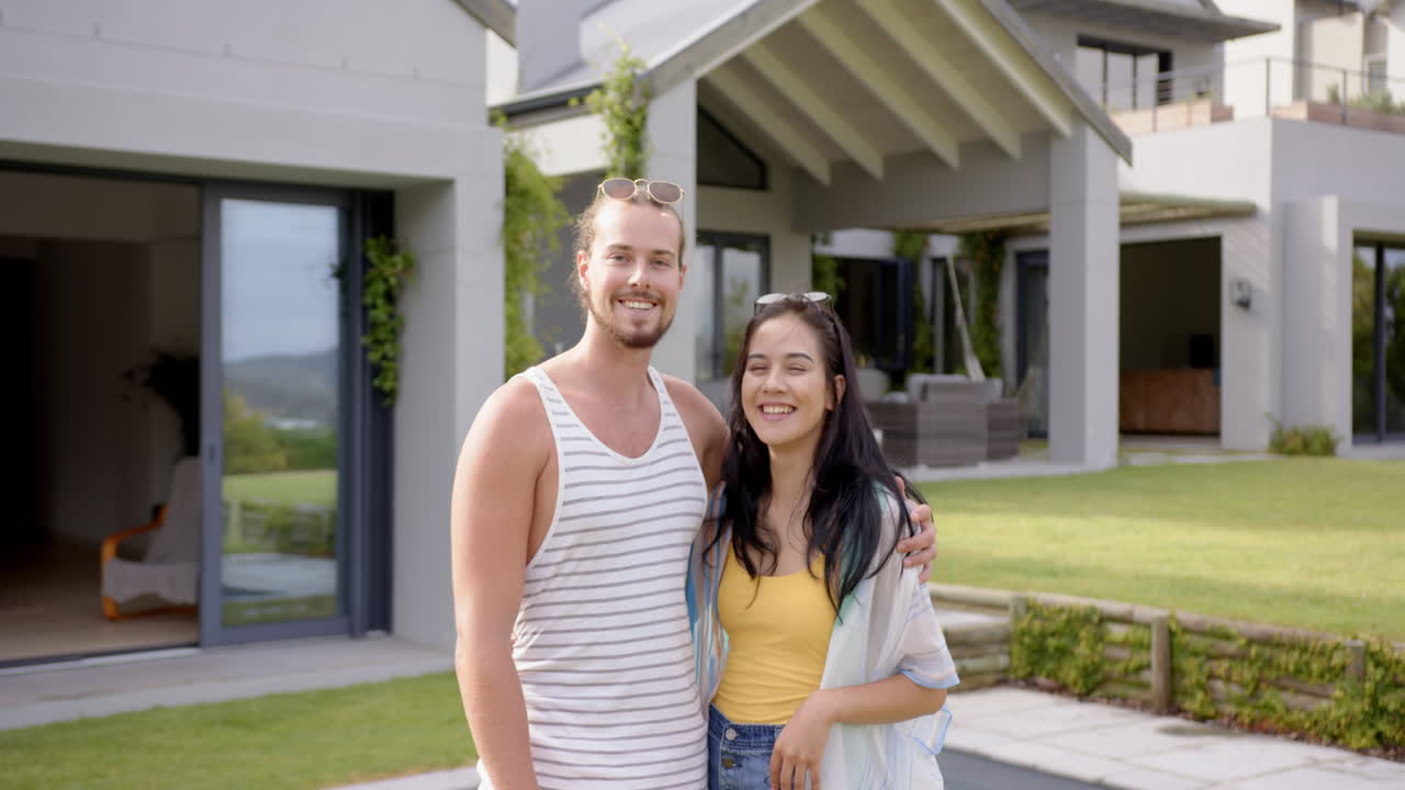Una pareja diversa sonríe fuera de una casa moderna en su jardín trasero en casa