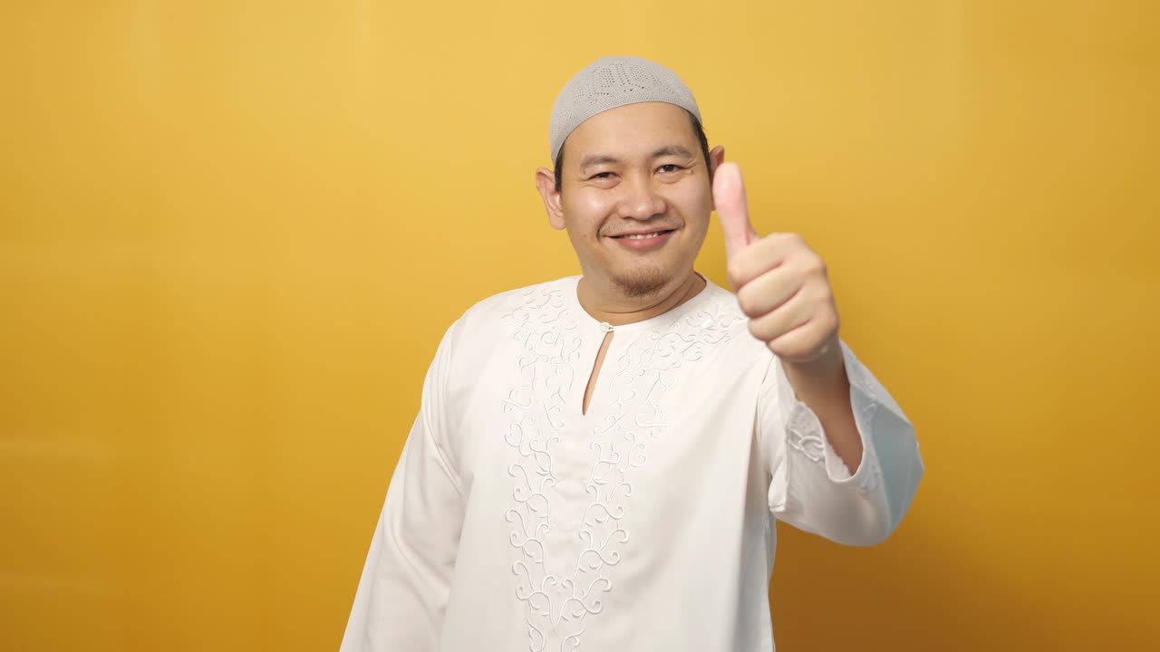 joven musulmán asiático feliz muestra el pulgar hacia arriba gesto, sonrisa cara feliz, aprobado ok signo, contra fondo amarillo