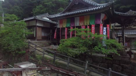 aerial view rises over a small japanese village, revealing a shrine and lush forested hill