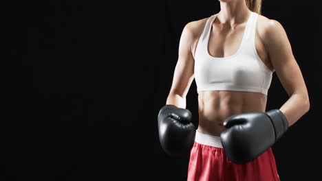 joven mujer caucásica boxeadora en equipo de boxeo posa con confianza sobre un fondo negro