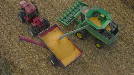 un agricultor del medio oeste cosechando un campo de maíz con una cosechadora, un tractor y un vagón de barrena
