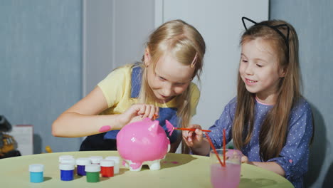 Two-Girls-Girlfriends-Paint-A-Piggy-Bank-Together-Have-Fun-4K-Video