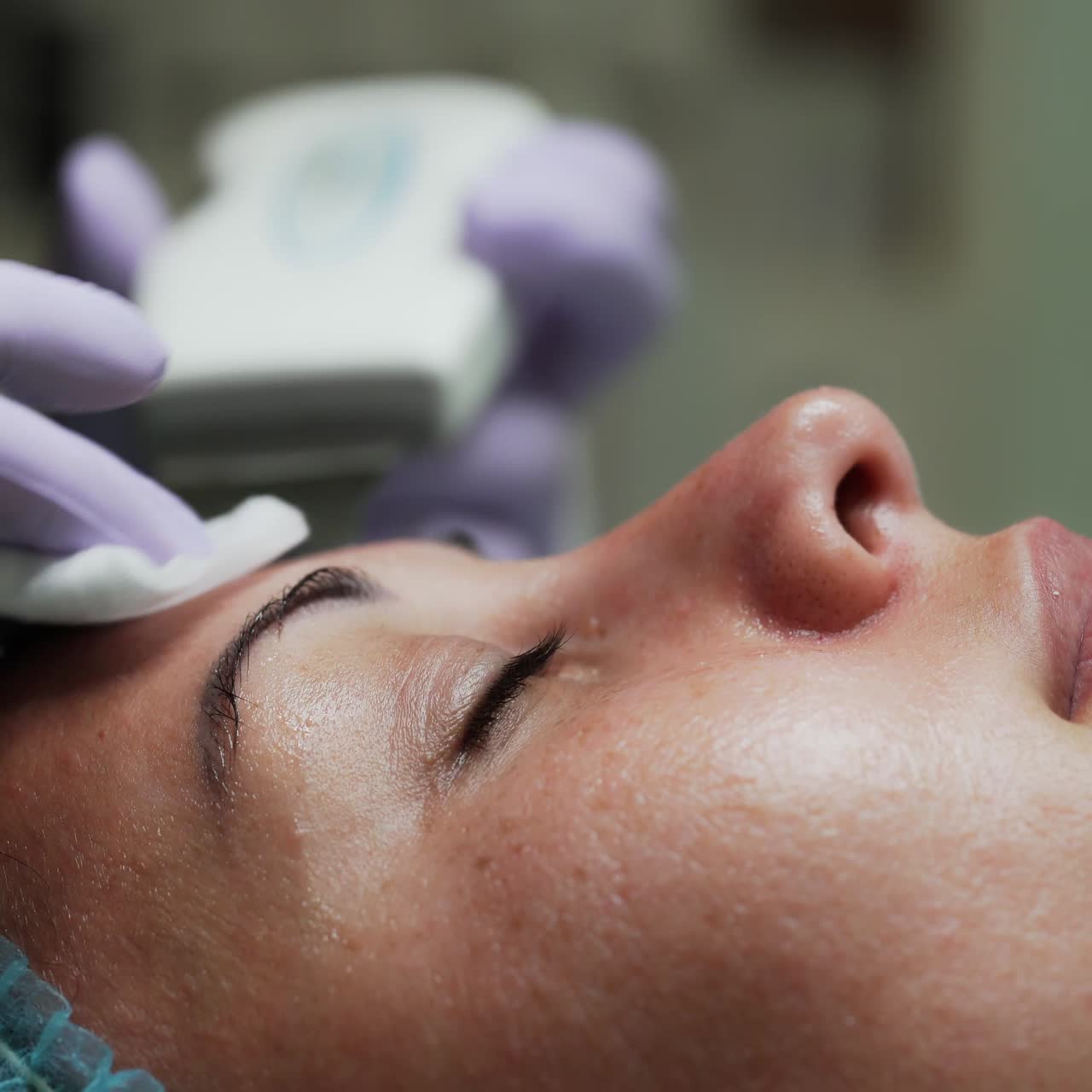 Ultrasonic face skin scrubber is moved by the female face. Cosmetologist holds the sponge in other hand using it to clean up. Close up