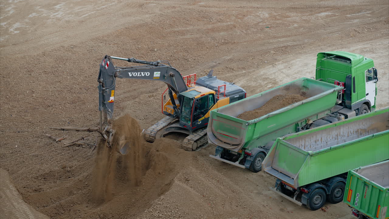 Excavator digging and filling green trucks at an active construction site. Preparatory work on a construction site. Excavator Loading Dirt into Truck. Groundwork and Site Preparation. Sitework