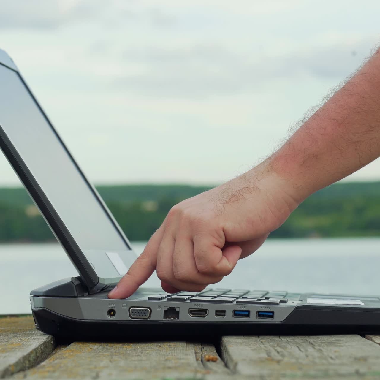 Man's hands using laptop computer. Young man sitting on a wharf and using a notebook