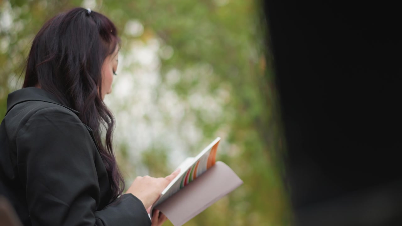 Primo piano di una donna che tiene in mano e rivede un documento all'aperto. La donna esamina la carta, girando le pagine per controllare le informazioni, contro una morbida luce naturale con vegetazione sullo sfondo.