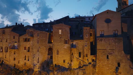 aerial drone view of the hilltop medieval town of pitigliano, tuscany at dusk, close-up with blinking lights, old buildings, and twilight sky, in 4k