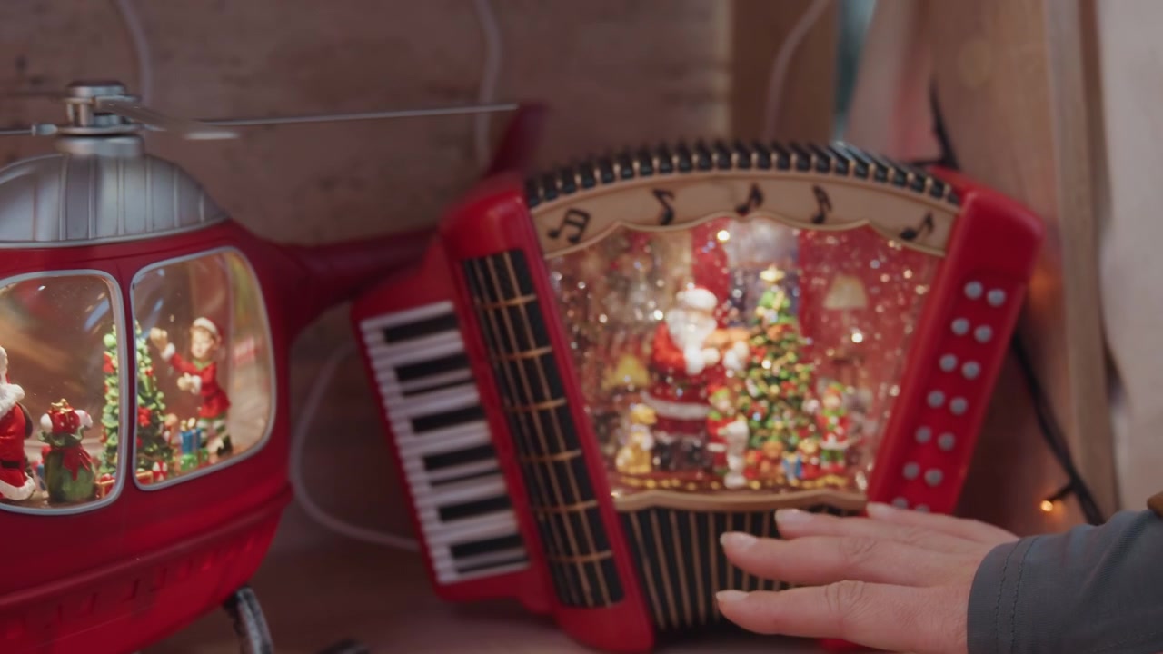 Rode helikopter sneeuwbol op een plank, hand van een blanke vrouw reikt om de gloeiende kerstman scène aan te raken in een vintage rood ornament, accordeon en radiospeelgoed in de buurt, warme lichten en glitters creëren een gezellige nostalgische sfeer.