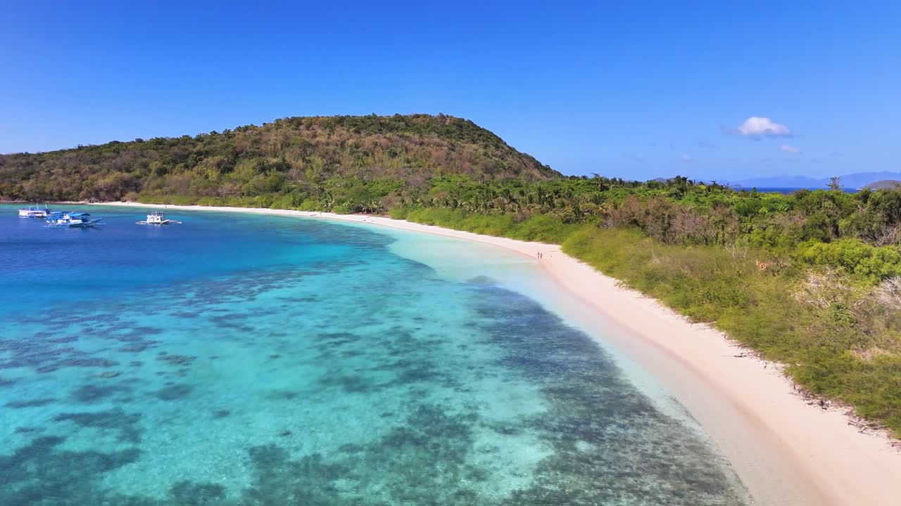 Aerial view of Ditaytayan Island in the Philippines, featuring white sand beach, turquoise waters, coral reefs, and lush hillside vegetation under clear blue skies