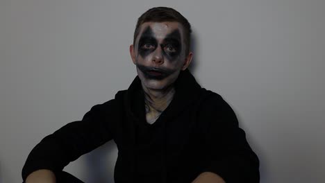 young caucasian man with black clown halloween makeup sitting down and talking to the camera