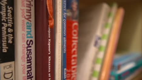 un primer plano de una plataforma rodante siguiendo la estantería de una biblioteca, los títulos visibles en el lomo de los respectivos libros